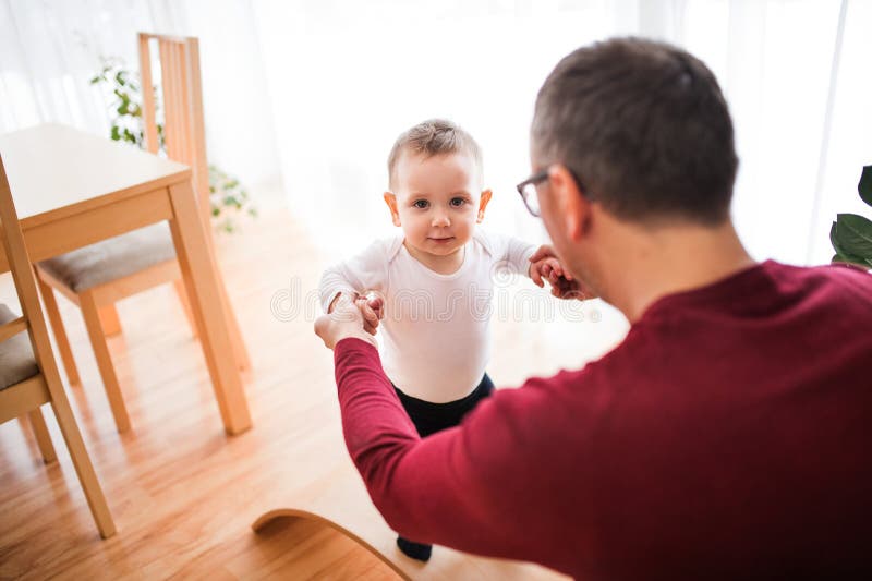 Pappa leker med en liten son som håller handen och hjälper till med första steget. arkivfoton