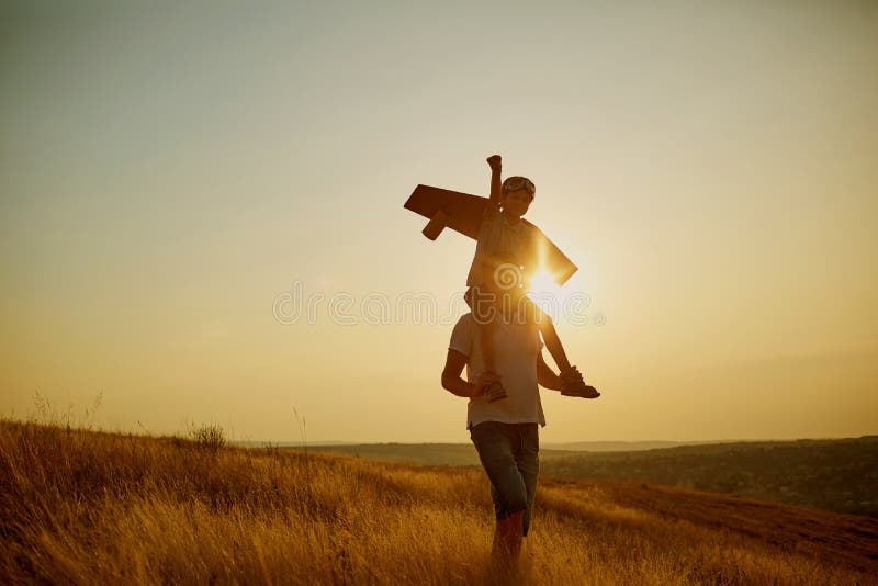 Papà con suo figlio in un vestito pilota del ` s al tramonto in natura fotografie stock libere da diritti Papà con suo figlio in un vestito pilota del ` s al tramonto in natura fotografie stock libere da diritti