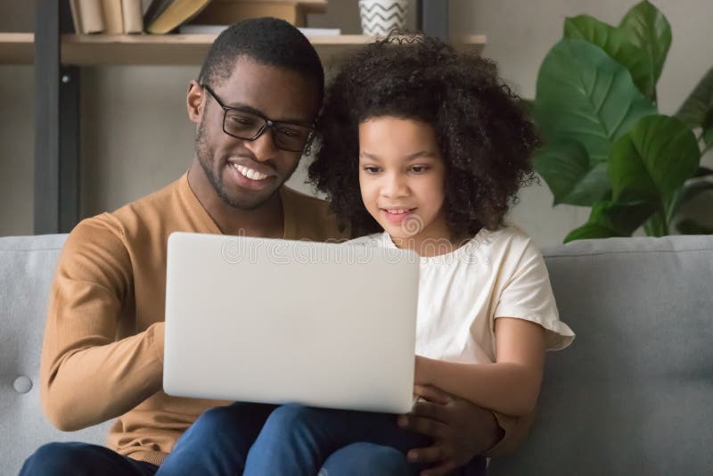 Papà nero sorridente e figlia usano il portatile a casa