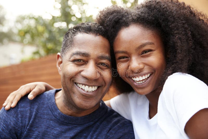 Middle aged black dad and teenage daughter embracing and smiling to camera, close up. Middle aged black dad and teenage daughter embracing and smiling to camera, close up