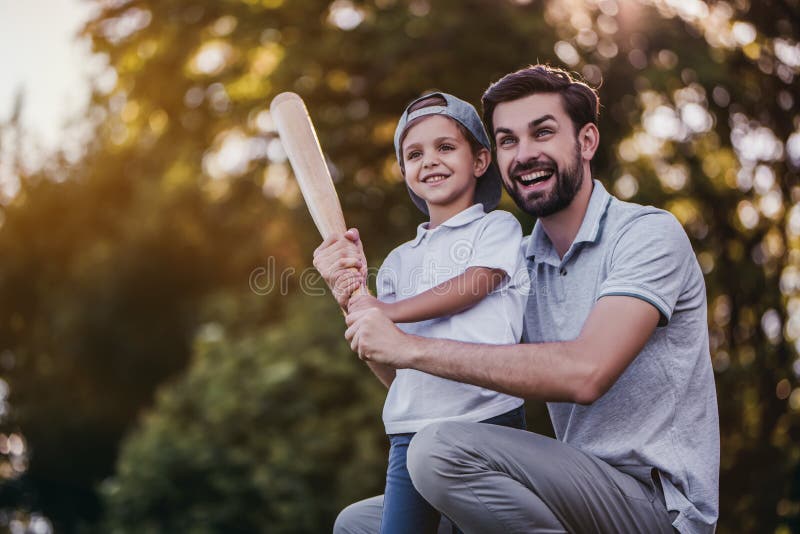 Handsome dad with his little cute sun are playing baseball on green grass lawn. Handsome dad with his little cute sun are playing baseball on green grass lawn