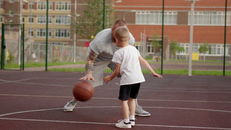 Papá e hijo juegan baloncesto juntos al aire libre en la cancha en la ciudad. almacen de metraje de vídeo