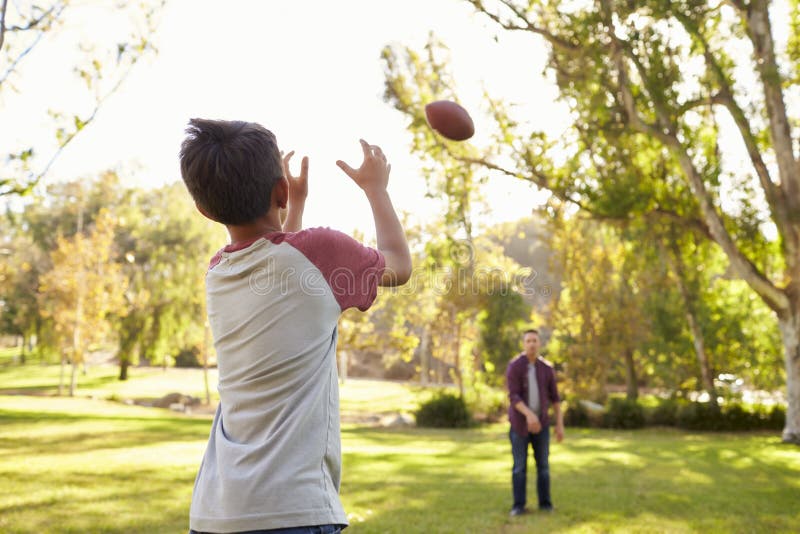Papá e hijo que lanzan fútbol americano el uno al otro en parque fotos de archivo Papá e hijo que lanzan fútbol americano el uno al otro en parque fotos de archivo
