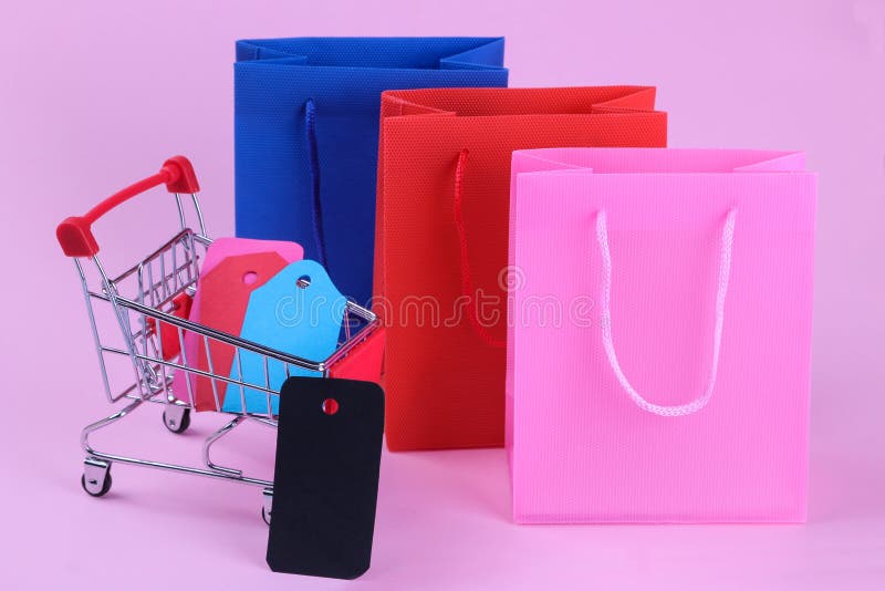 paquets pour des achats et un chariot à achats à l'intérieur avec différentes étiquettes et prix à payer sur un fond rose lumineu photographie stock libre de droits paquets pour des achats et un chariot à achats à l'intérieur avec différentes étiquettes et prix à payer sur un fond rose lumineu photographie stock libre de droits