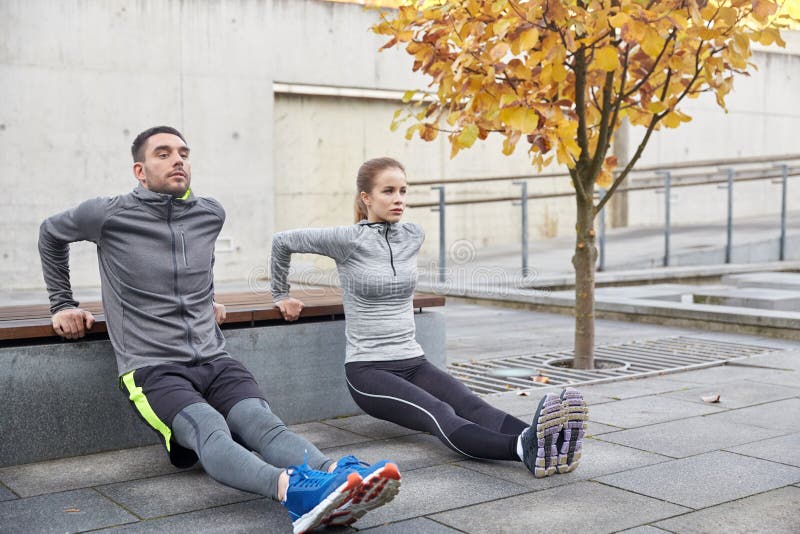 Fitness, sport, exercising, training and people concept - couple doing triceps dip exercise on city street bench. Fitness, sport, exercising, training and people concept - couple doing triceps dip exercise on city street bench