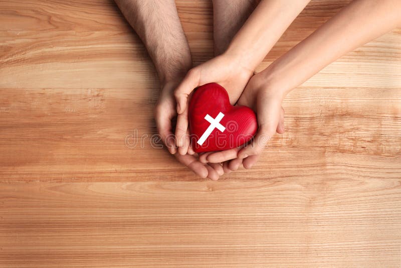 Couple holding heart with cross symbol on wooden background, top view. Christian religion. Couple holding heart with cross symbol on wooden background, top view. Christian religion