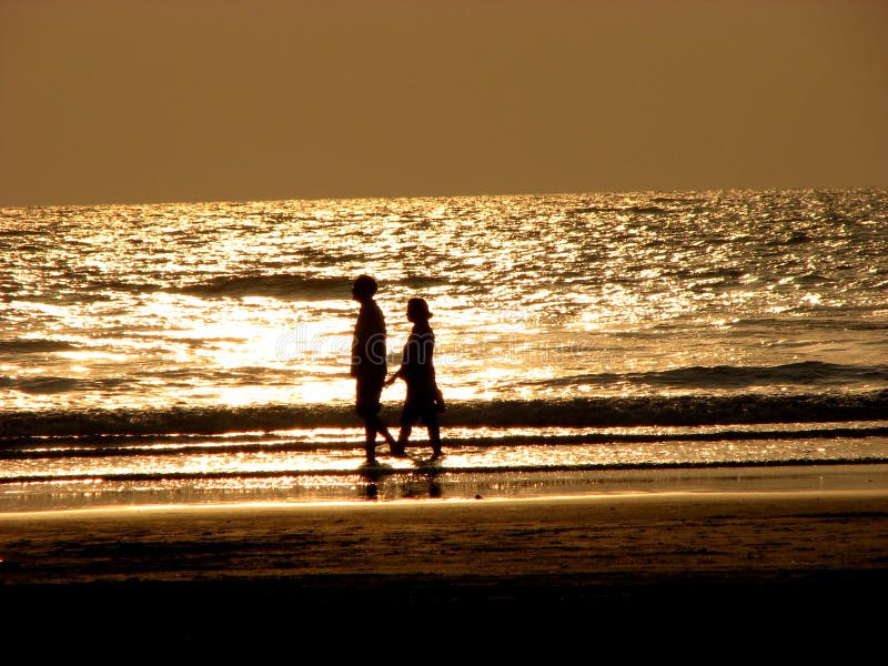 A couple walks down the beach at the golden time in the evening. A couple walks down the beach at the golden time in the evening