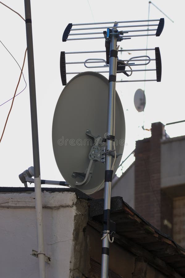 Backlit image of a satellite dish next to a conventional digital terrestrial television antenna hooked to a building wall. Backlit image of a satellite dish next to a conventional digital terrestrial television antenna hooked to a building wall