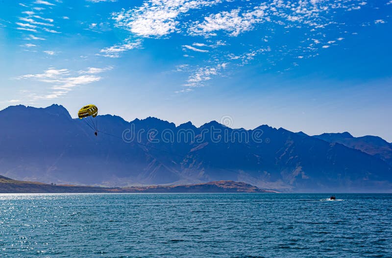 Parasailing on lake Wakatipu Queenstown New Zealand. Parasail is shown against the Southern Alps background with the boat in turquoise water of lake Wakatipu. Nice blue skyline. Parasailing on lake Wakatipu Queenstown New Zealand. Parasail is shown against the Southern Alps background with the boat in turquoise water of lake Wakatipu. Nice blue skyline.