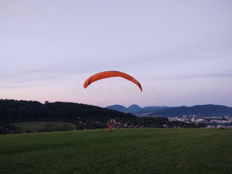 Padákový klzák lietajúci na padáku pri západe slnka na lúke.