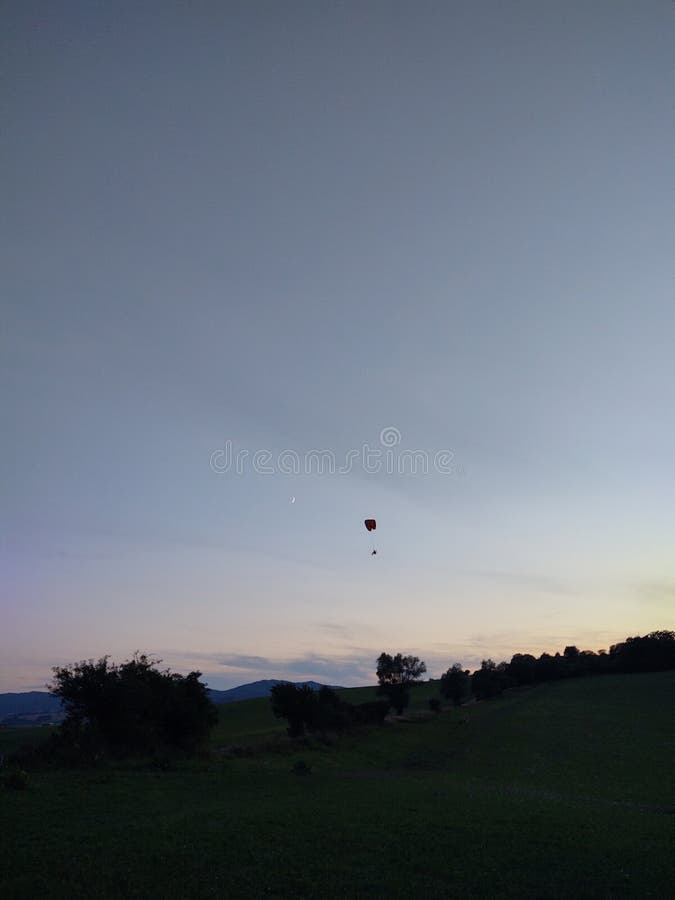 Paraglider flying on the parachute during sunset on the meadow.