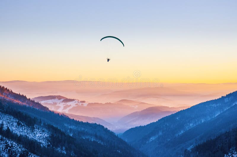 Paraglider silhouette flying over misty mountain valley in beautiful warm sunset colors - sport, active wallpapers full of freedom