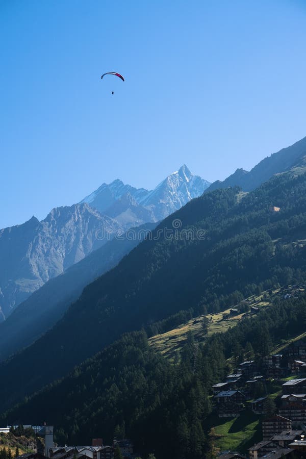 Paraglider soaring above a picturesque mountain landscape with clear blue sky stock images