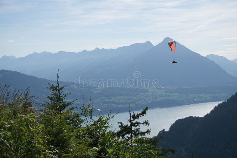 Paraglider soaring over a scenic mountain landscape with a lake view under a clear sky. stock photo