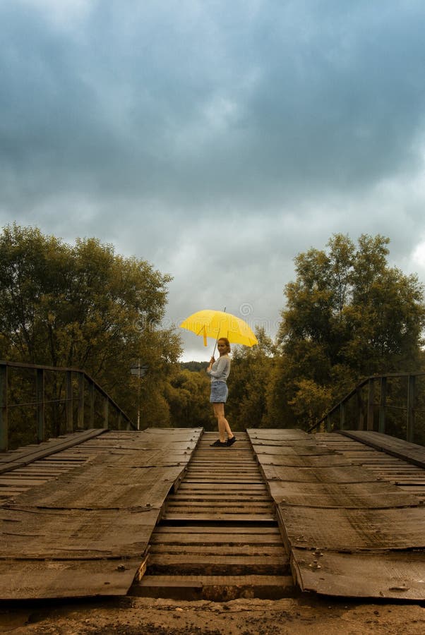 Paraguas hermoso del amarillo del control de la mujer y el caminar en un puente viejo en el campo debajo de la lluvia fotos de archivo libres de regalías Paraguas hermoso del amarillo del control de la mujer y el caminar en un puente viejo en el campo debajo de la lluvia fotos de archivo libres de regalías