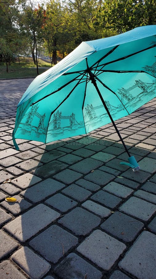 Parapluie bleu humide après la pluie debout sur des dalles de pierre. Parapluie de couleur turquoise placé sur le pavé de tuiles en pierre humide après la pluie. Parapluie bleu ouvert avec le modèle d'impression d'art de tower bridge de Londres