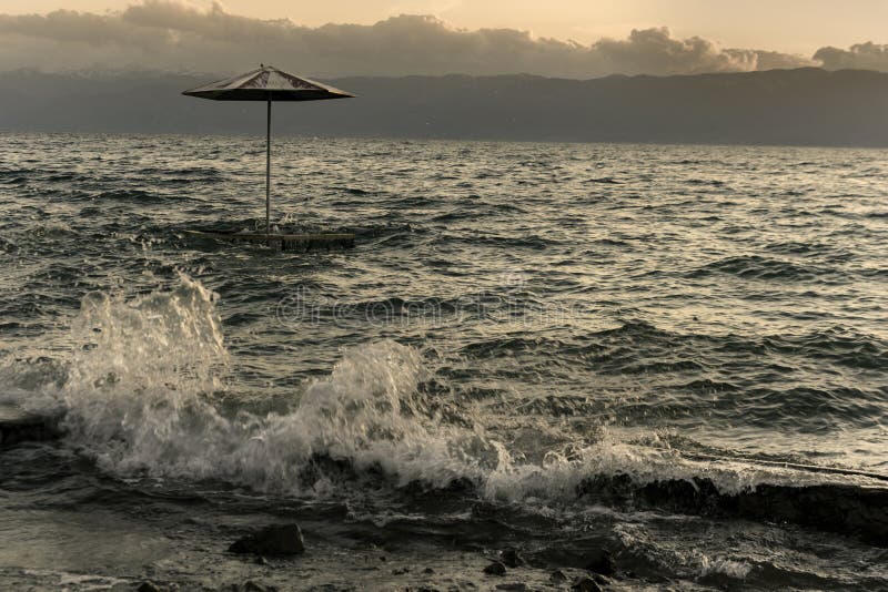 Parapluie de plage dans le lac Ohrid au coucher du soleil de temps orageux photos libres de droits Parapluie de plage dans le lac Ohrid au coucher du soleil de temps orageux photos libres de droits