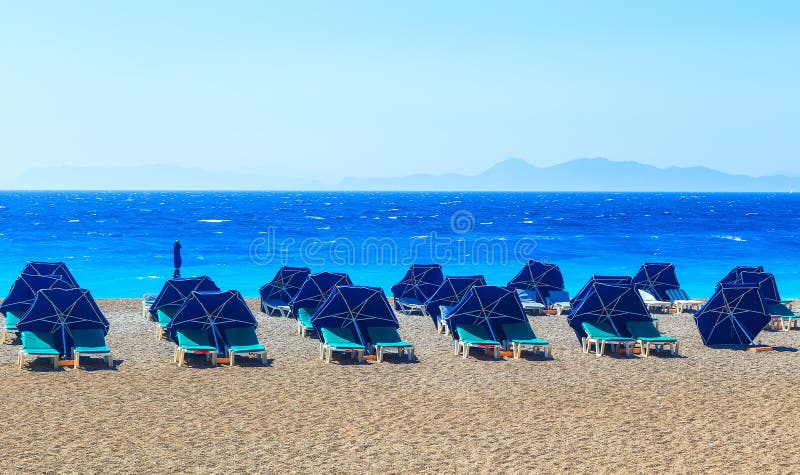 Parapluies de plage colorés avec le caillou et l'île de chaises de plate-forme dans la distance image stock Parapluies de plage colorés avec le caillou et l'île de chaises de plate-forme dans la distance image stock