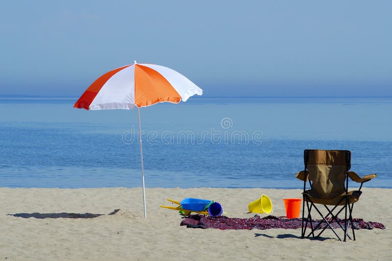 A beach scene with colourful umbrellas, beach toys, beach blanket, and beach chair. A beach scene with colourful umbrellas, beach toys, beach blanket, and beach chair.