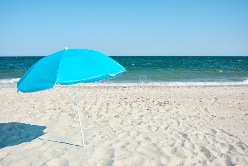 Turquoise beach umbrella by sea shore. Sunny hot day on the sandy beach. Sand with sea. Turquoise beach umbrella by sea shore. Sunny hot day on the sandy beach. Sand with sea.