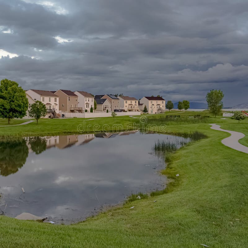 Parc de voisinage scénique de cadre carré avec un étang brillant et voie sous un ciel obscurci photographie stock libre de droits Parc de voisinage scénique de cadre carré avec un étang brillant et voie sous un ciel obscurci photographie stock libre de droits