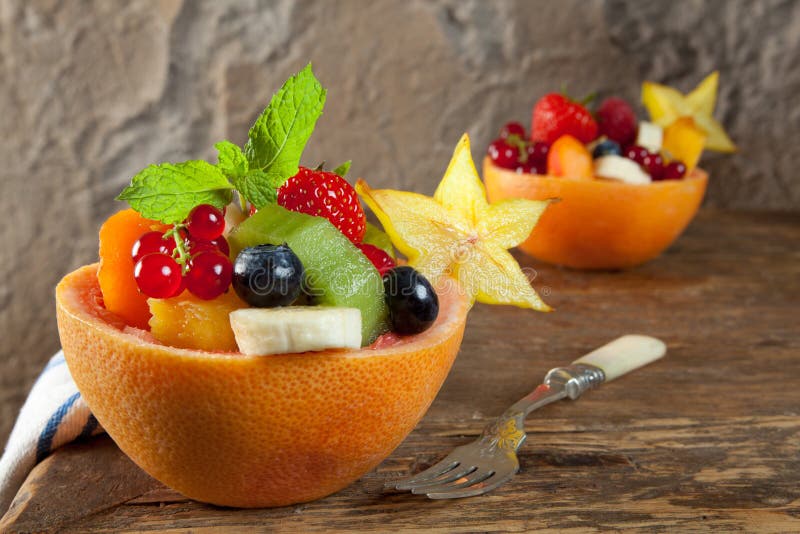 Two portions of fruit salad in grapefruit bowls on an antique table. Two portions of fruit salad in grapefruit bowls on an antique table