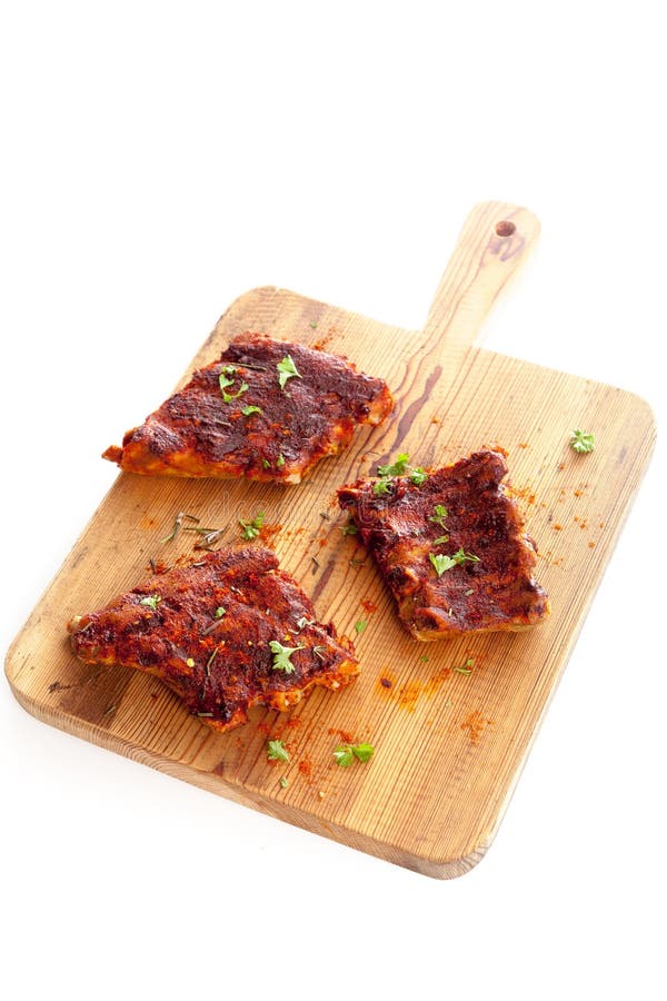Portions of spicy BBQ ribs seasoned with aromatic condiments and fresh herbs on a wooden chopping board isolated on white. Portions of spicy BBQ ribs seasoned with aromatic condiments and fresh herbs on a wooden chopping board isolated on white