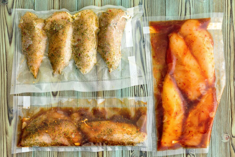 Vacuum packed portions of lean chicken breast with assorted marinades and seasoned with spices and herbs ready for freezing or sous-vide cooking on rustic wood. Vacuum packed portions of lean chicken breast with assorted marinades and seasoned with spices and herbs ready for freezing or sous-vide cooking on rustic wood