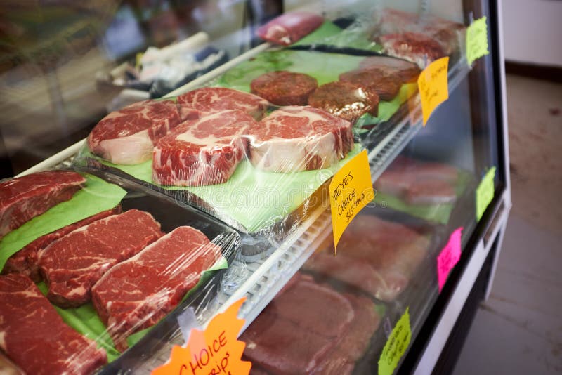 Assorted portions of fresh prime meat in a glass counter display in a butchery with prices. Assorted portions of fresh prime meat in a glass counter display in a butchery with prices