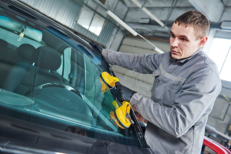 Glazier repairman mechanic worker replaces windshield or windscreen on a car in automobile workshop garage. Glazier repairman mechanic worker replaces windshield or windscreen on a car in automobile workshop garage