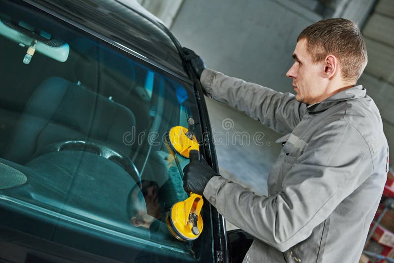 Glazier repairman mechanic worker replaces windshield or windscreen on a car in automobile workshop garage. Glazier repairman mechanic worker replaces windshield or windscreen on a car in automobile workshop garage