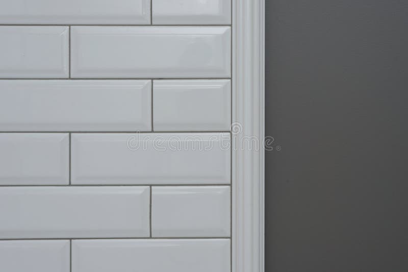 A parede pintada cinza, peça da parede é tijolo lustroso branco pequeno coberto das telhas, telhas decorativas cerâmicas do molde fotografia de stock royalty free A parede pintada cinza, peça da parede é tijolo lustroso branco pequeno coberto das telhas, telhas decorativas cerâmicas do molde fotografia de stock royalty free