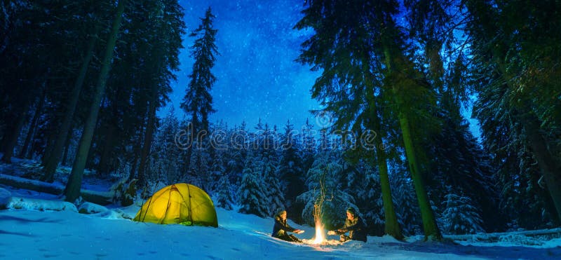 Pareja acampar con fogata y carpa al aire libre en el bosque invernal foto de archivo