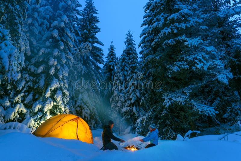 Pareja acampar con fogata y carpa al aire libre en el bosque invernal foto de archivo