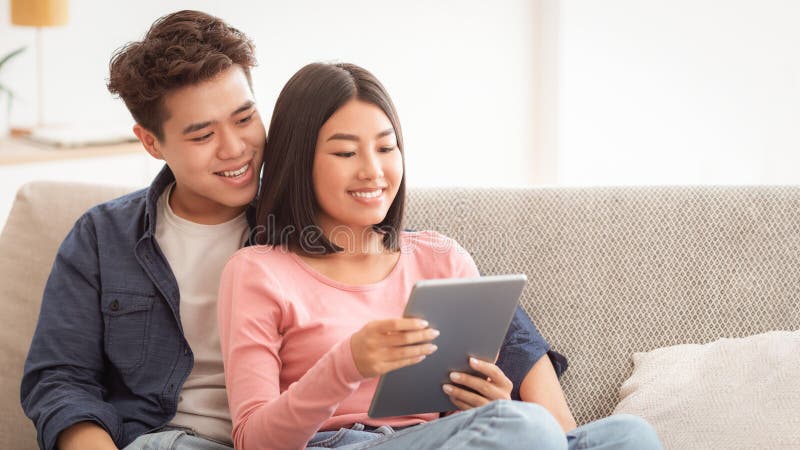 Pareja Asiática Alegre Con Tableta Digital Sentada En El Sillón Interior fotos de archivo libres de regalías