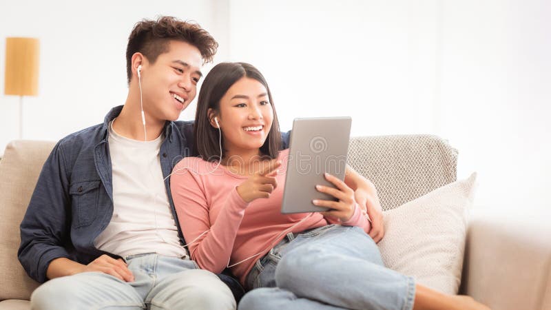 Pareja asiática alegre usando tableta digital navegando por Internet en casa imagenes de archivo