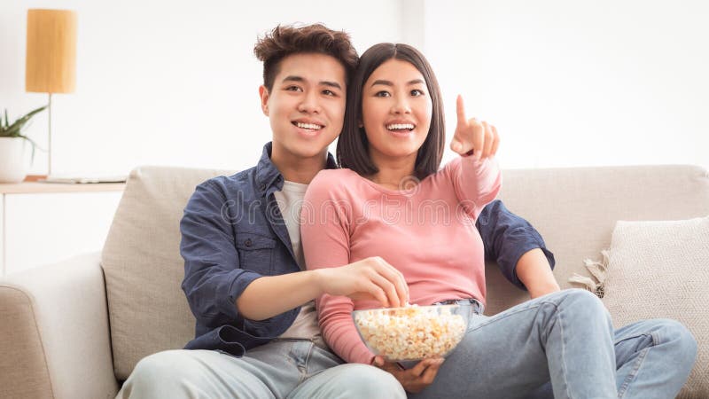 Pareja Asiática Viendo La Televisión Y Comiendo Popcorn En Casa fotografía de archivo libre de regalías