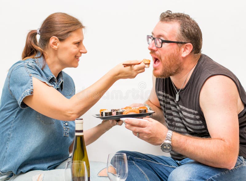 Pareja atractiva comiendo comida japonesa juntos en el sofá. pareja relajándose en el sofá de casa comiendo comida exótica en un foto de archivo libre de regalías