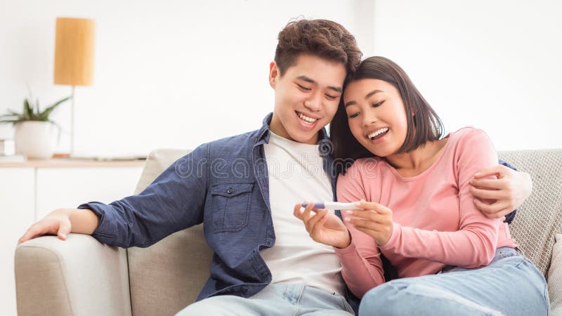 Pareja china con prueba de embarazo positiva sentada en casa fotos de archivo libres de regalías