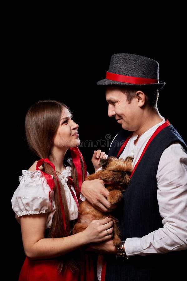 Pareja con ropa étnica nacional con perro pequeño en las manos posando en un estudio de fondo negro. joven, hombre o niño imágenes de archivo libres de regalías
