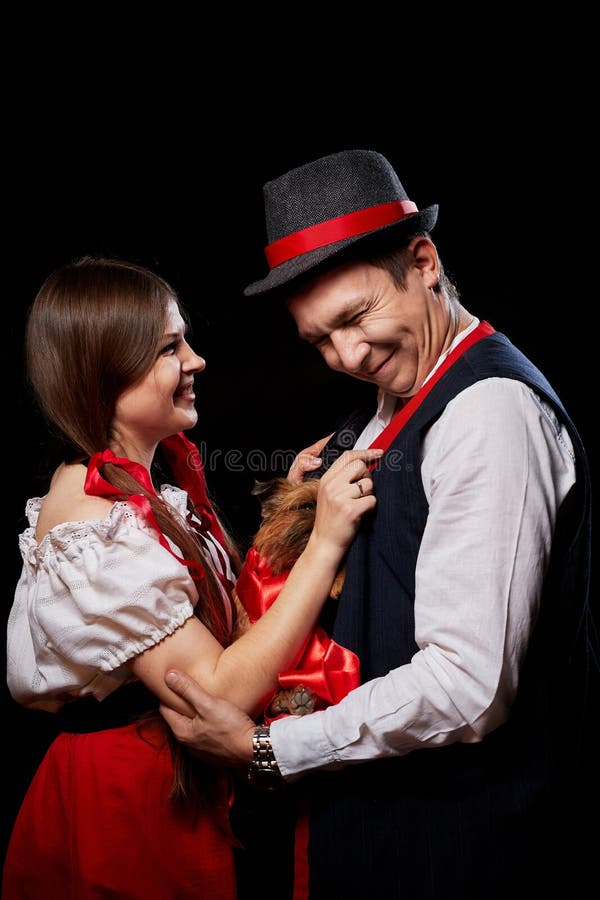 Pareja con ropa étnica nacional con perro pequeño en las manos posando en un estudio de fondo negro. joven, hombre o niño foto de archivo