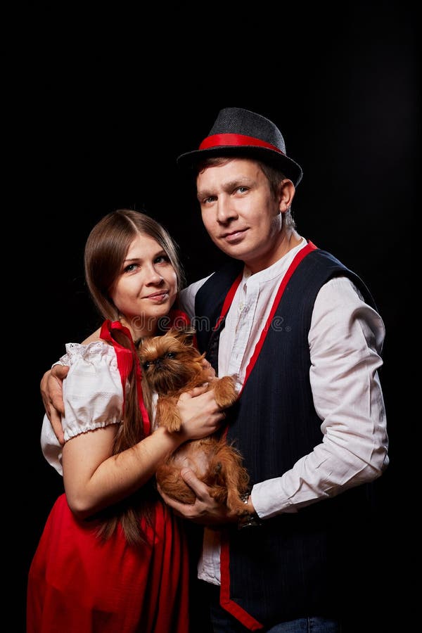 Pareja con ropa étnica nacional con perro pequeño en las manos posando en un estudio de fondo negro. joven, hombre o niño imagen de archivo