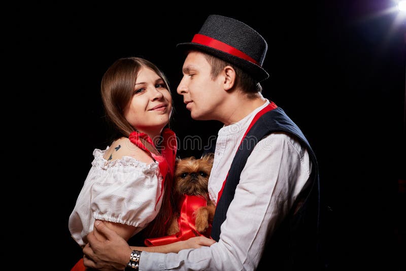 Pareja con ropa étnica nacional con perro pequeño en las manos posando en un estudio de fondo negro. joven, hombre o niño fotos de archivo