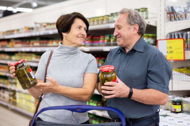 Pareja de ancianos casados eligiendo pepinos enlatados juntos en la sección de compras del supermercado imágenes de archivo libres de regalías