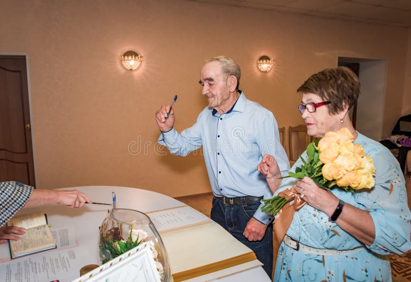 Pareja de ancianos rusos en sus 70 años celebra su 50 aniversario de bodas con la firma de documentos en una oficina de registro. imagen de archivo libre de regalías