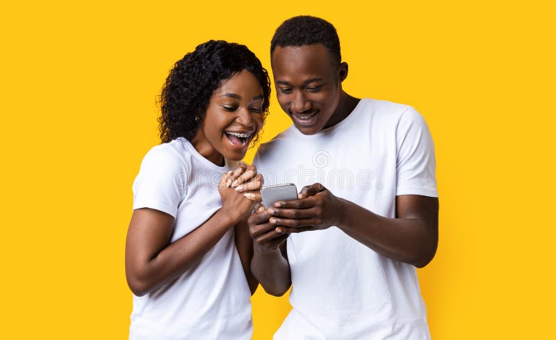 Pareja de negros emocionada mirando la pantalla del teléfono móvil imagen de archivo libre de regalías