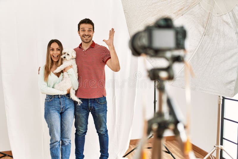 Pareja de novio y novia con perro posando como modelo en el estudio de fotografía celebrando la victoria con una sonrisa feliz y e fotografía de archivo libre de regalías