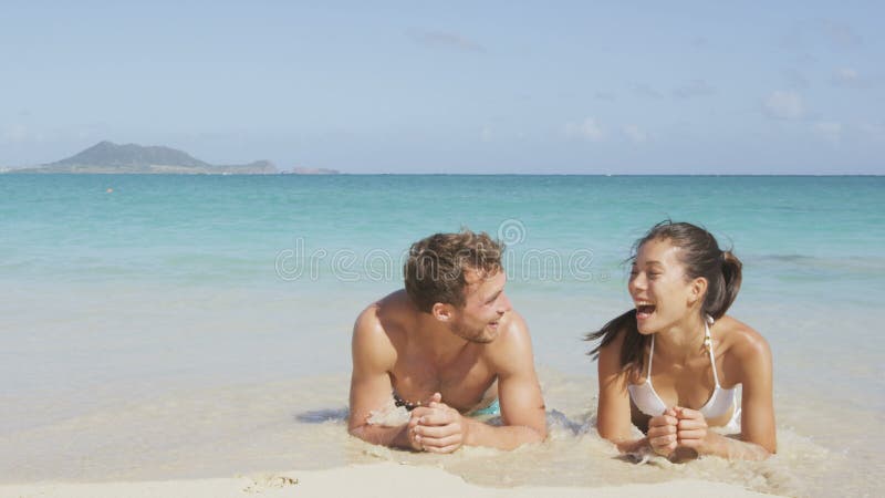 Pareja de playa riendo divirtiéndose salpicando agua almacen de metraje de vídeo