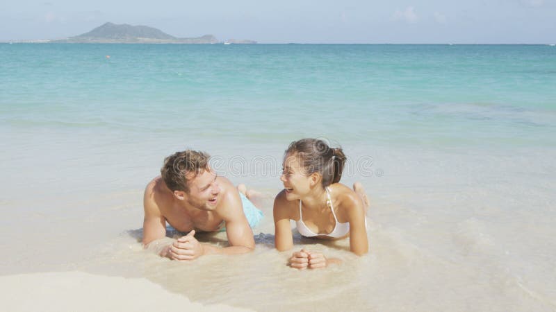 Pareja de vacaciones riéndose relajándose en el bronceado de la playa almacen de video