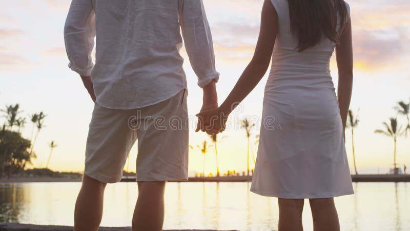 Pareja en manos enamoradas disfrutando de vacaciones románticas al atardecer en la playa